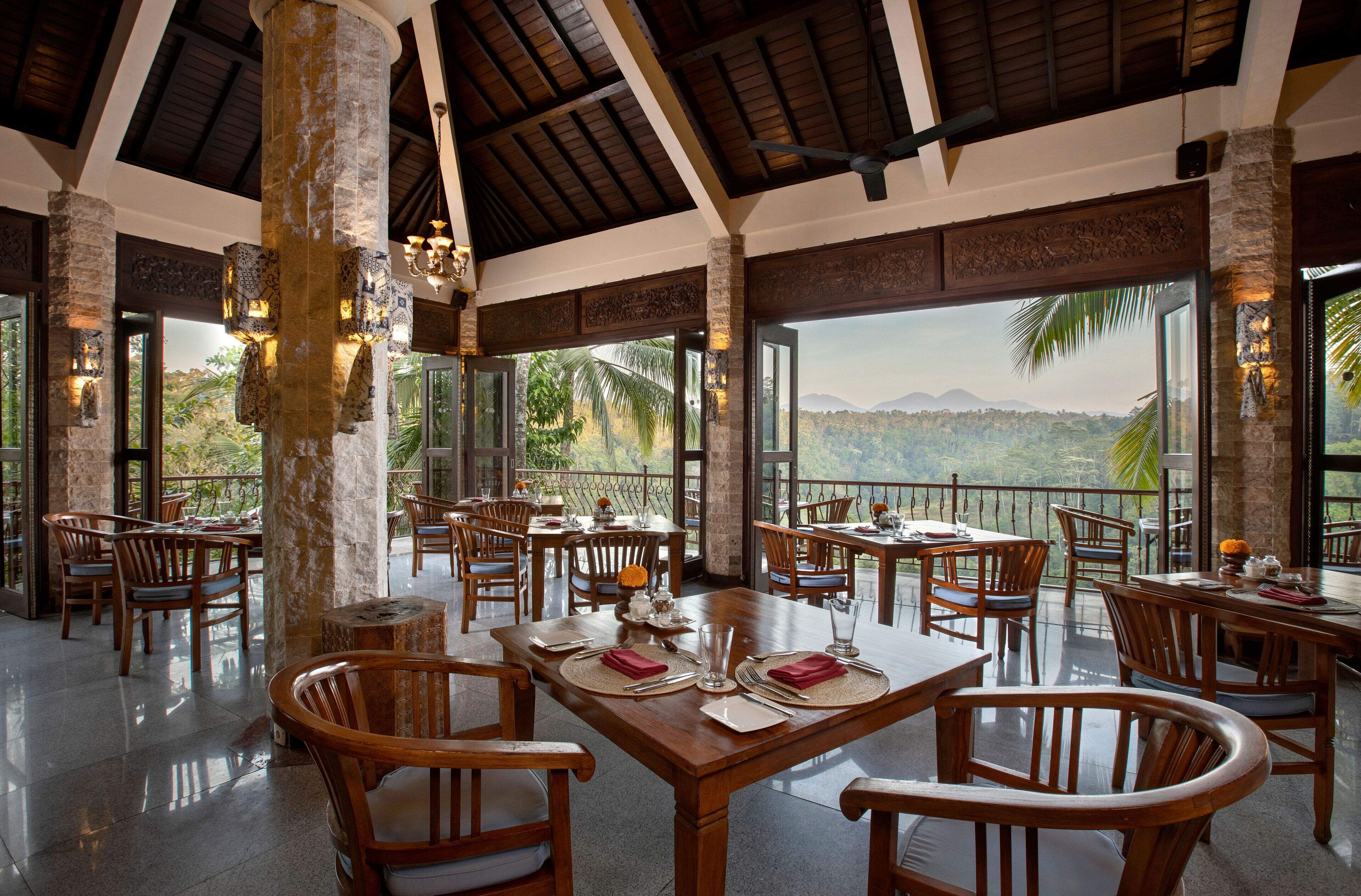 Un comedor amplio con mesas y sillas de madera, y ventanas grandes que ofrecen vistas al paisaje.