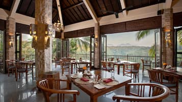 A spacious dining area with wooden tables and chairs, large windows offering a view of the landscape.