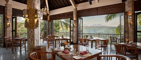 Un comedor amplio con mesas y sillas de madera, y ventanas grandes que ofrecen vistas al paisaje.