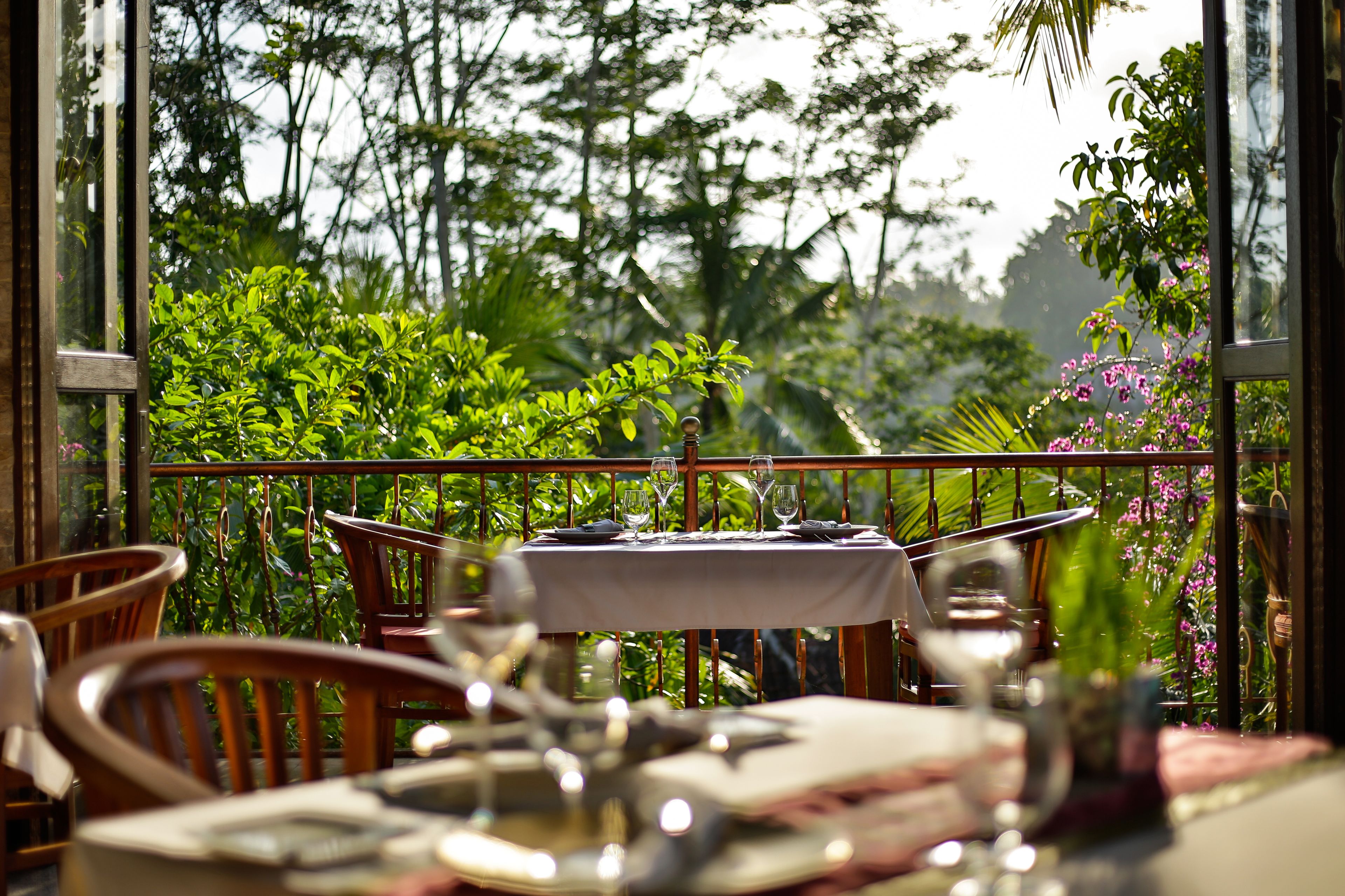 An outdoor dining area with a table set for two, surrounded by lush greenery and a view of the forest.