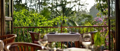 An outdoor dining area with a table set for two, surrounded by lush greenery and a view of the forest.
