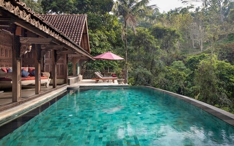 Una piscina con agua cristalina, rodeada de exuberante vegetación y una estructura de madera con intrincados grabados.