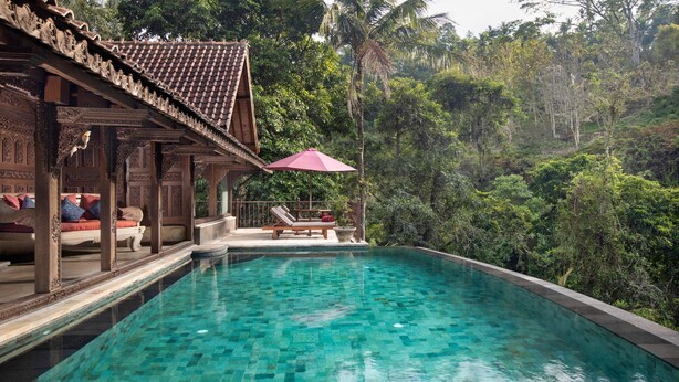 Una piscina con agua cristalina, rodeada de exuberante vegetación y una estructura de madera con intrincados grabados.