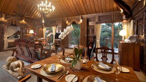 Un comedor con una mesa de madera dispuesta para cuatro personas, rodeada de sillas ornamentadas, un candelabro y vistas al exterior.