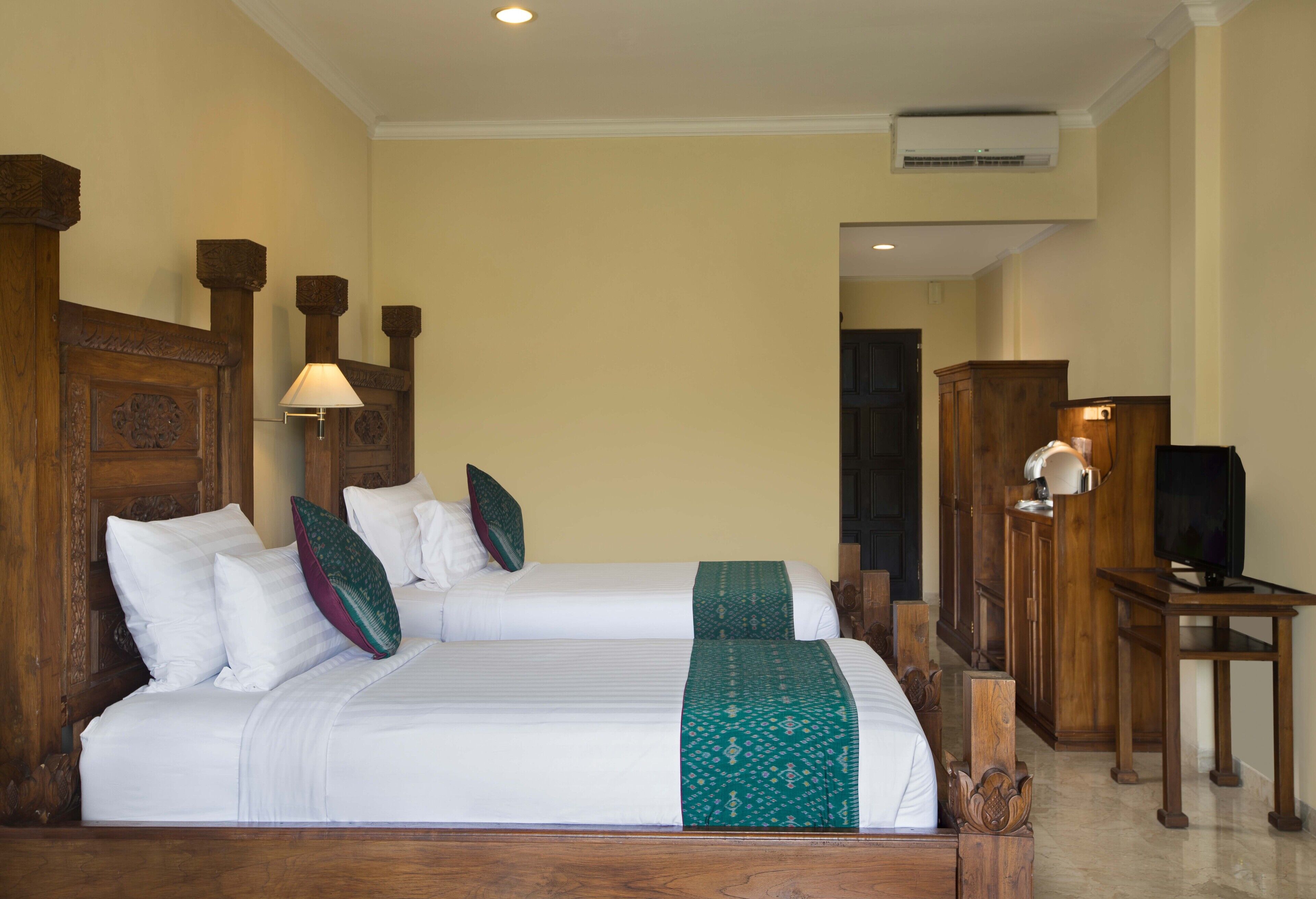 A hotel room with two beds, wooden headboards, a television on a wooden table, and a cabinet.