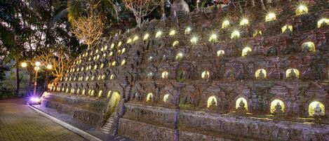 A stone staircase with multiple niches, each illuminated by lights, leading up to a statue.