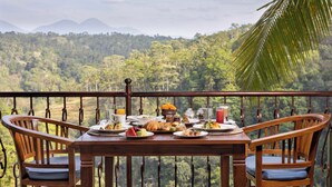 Una mesa de madera dispuesta con alimentos para el desayuno y una vista panorámica de un bosque exuberante y montañas.