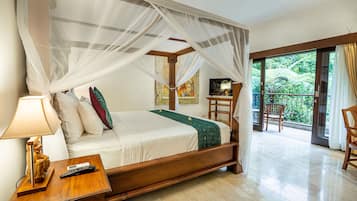 A spacious bedroom with a four-poster bed, a nightstand with a lamp, a chair, and a view of lush greenery through the balcony doors.