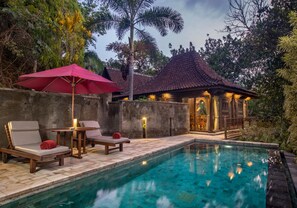A pool area with lounge chairs and a red umbrella, surrounded by a stone wall and tropical vegetation. - Ayung Resort Ubud (Ubud)