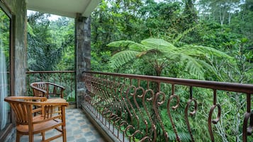 Un balcón con baranda de hierro forjado, sillas de madera y vistas a una exuberante vegetación tropical.