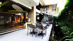 Amplio espacio interior con varias mesas y sillas, una pequeña fuente de agua y una escalera que lleva a un nivel superior.