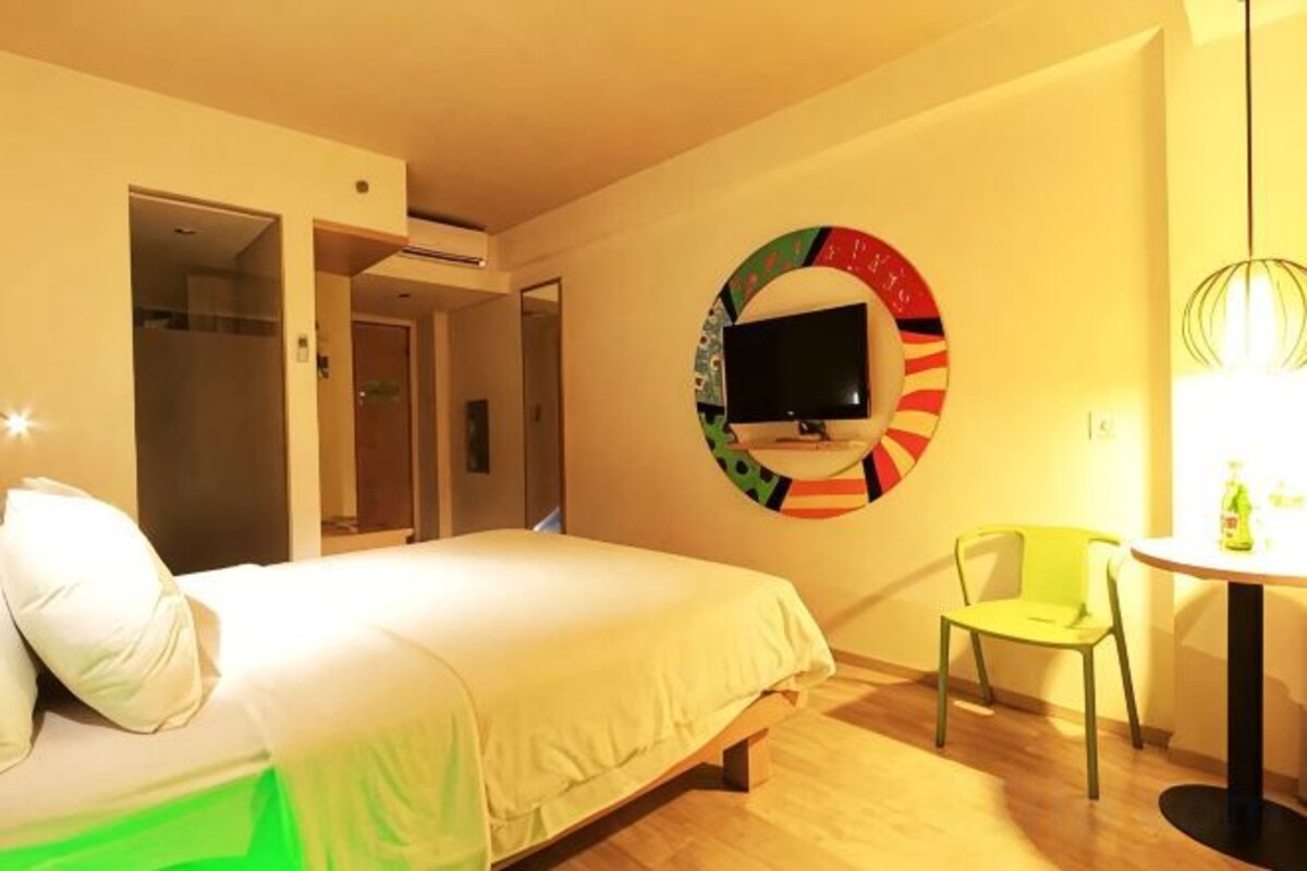 A hotel room with a bed, a chair, a table, and a TV mounted on the wall.