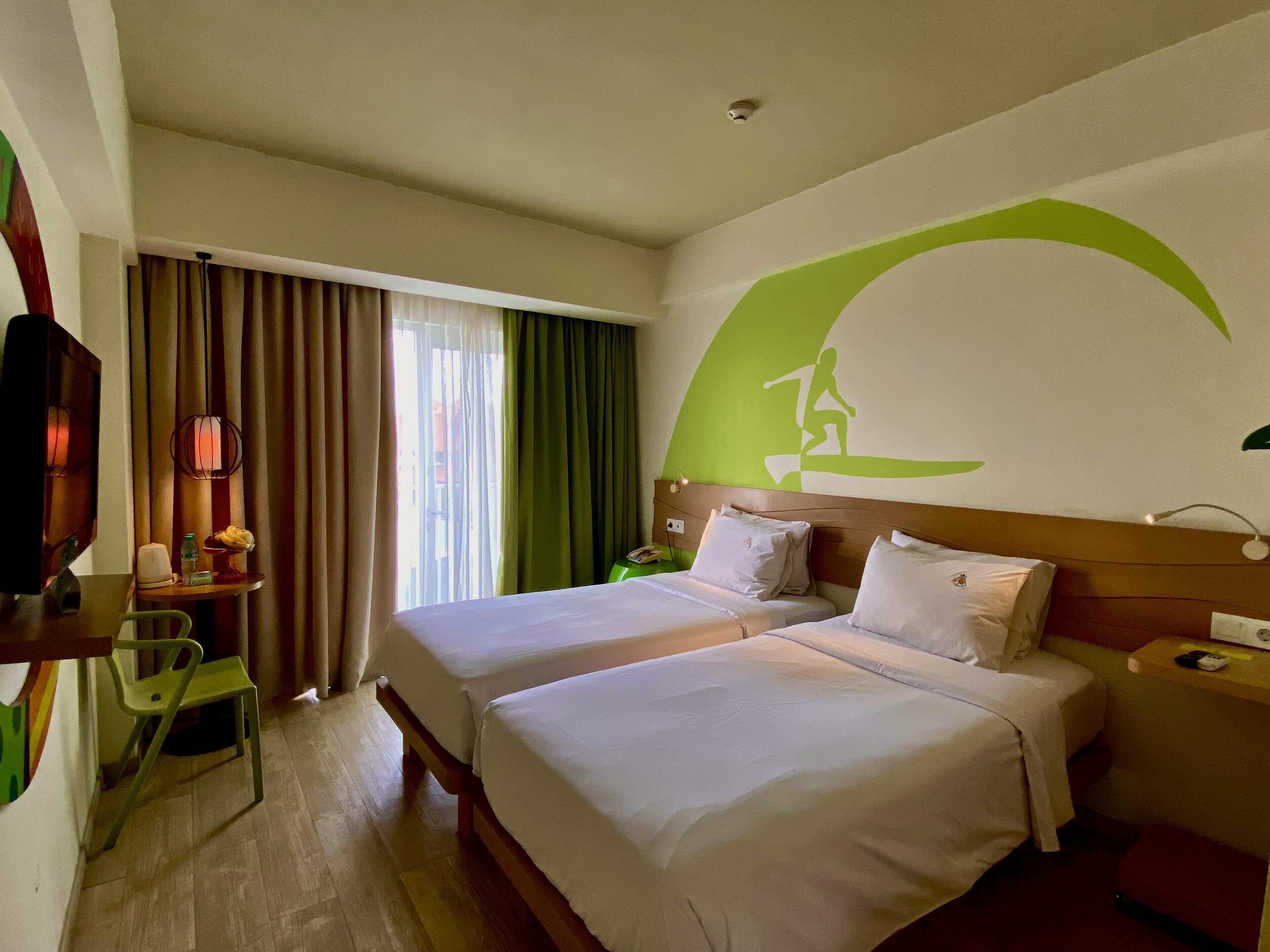 Una habitación de hotel con dos camas, un escritorio con silla, un televisor y una ventana con cortinas.