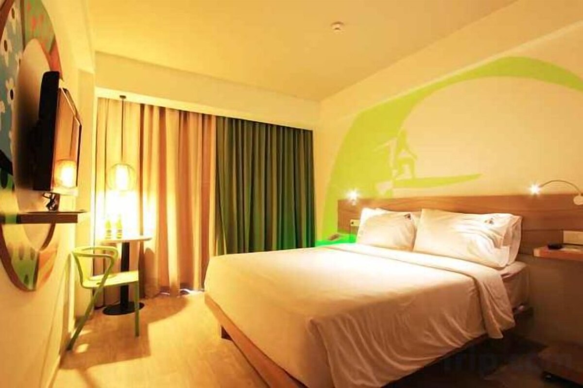 A hotel room with a bed, a desk with a chair, a television, and curtains.