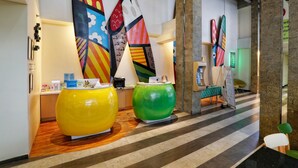 Un área de recepción con diseño moderno, que cuenta con un mostrador de recepción, arte abstracto y colorido en las paredes, y un patrón de piso a rayas.