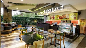 Un interior de cafetería con un letrero 'maxbistro', mesas, sillas, una barra y una exhibición de bebidas.
