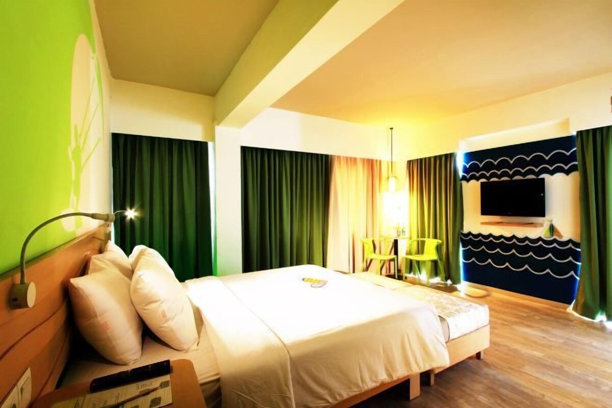 A hotel room with a bed, a desk, a chair, a TV, and a lamp.