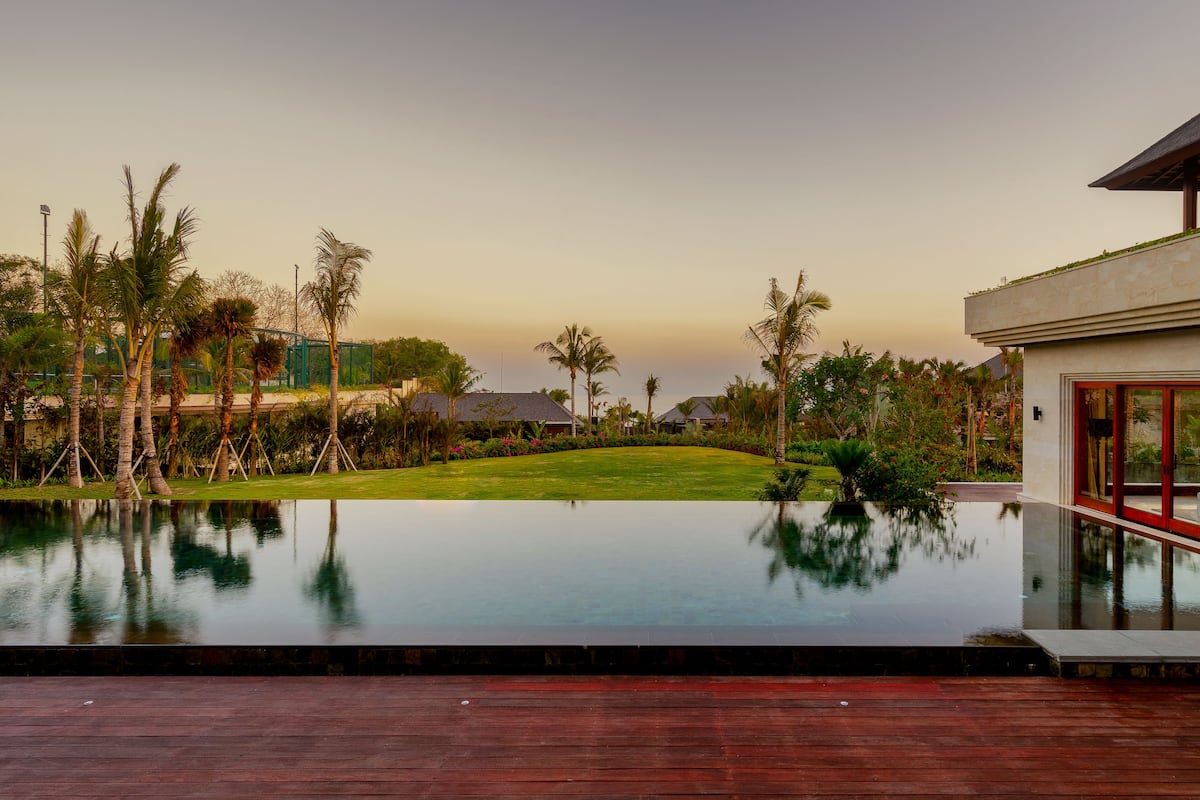 Un moderno resort con piscina, abundante vegetación y vista despejada al océano.