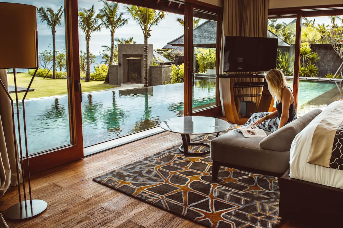 Una sala de estar moderna con un amplio ventanal con vistas a una piscina y jardín tropical.