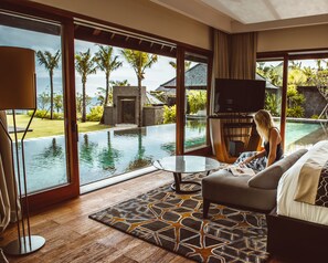 Una sala de estar moderna con un amplio ventanal con vistas a una piscina y jardín tropical.