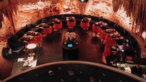A circular seating area with tables and chairs arranged around a central focal point, set against a cave-like interior with natural rock formations and lighting.