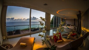 Una camera d'albergo moderna con un ampio balcone, una poltrona massaggiante, un divano e una reception.