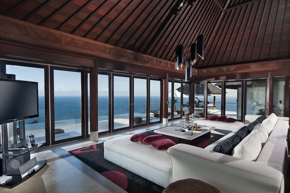 Una sala de estar moderna con un amplio ventanal con vistas al océano, un sofá blanco y un televisor de pantalla plana.