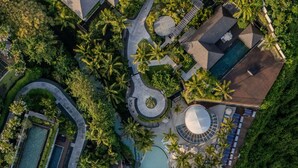 Una vista aerea di un resort con diverse piscine, palme e un litorale roccioso.