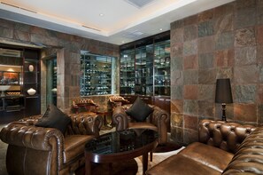 A luxurious living room with leather sofas, a glass coffee table, and a wine rack against a stone wall.