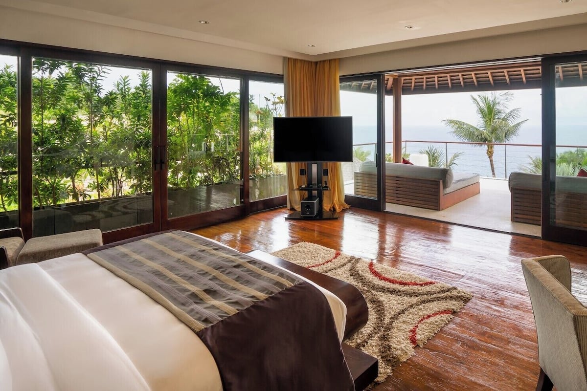 Un dormitorio amplio con una cama grande, televisión y balcón con vistas al océano.