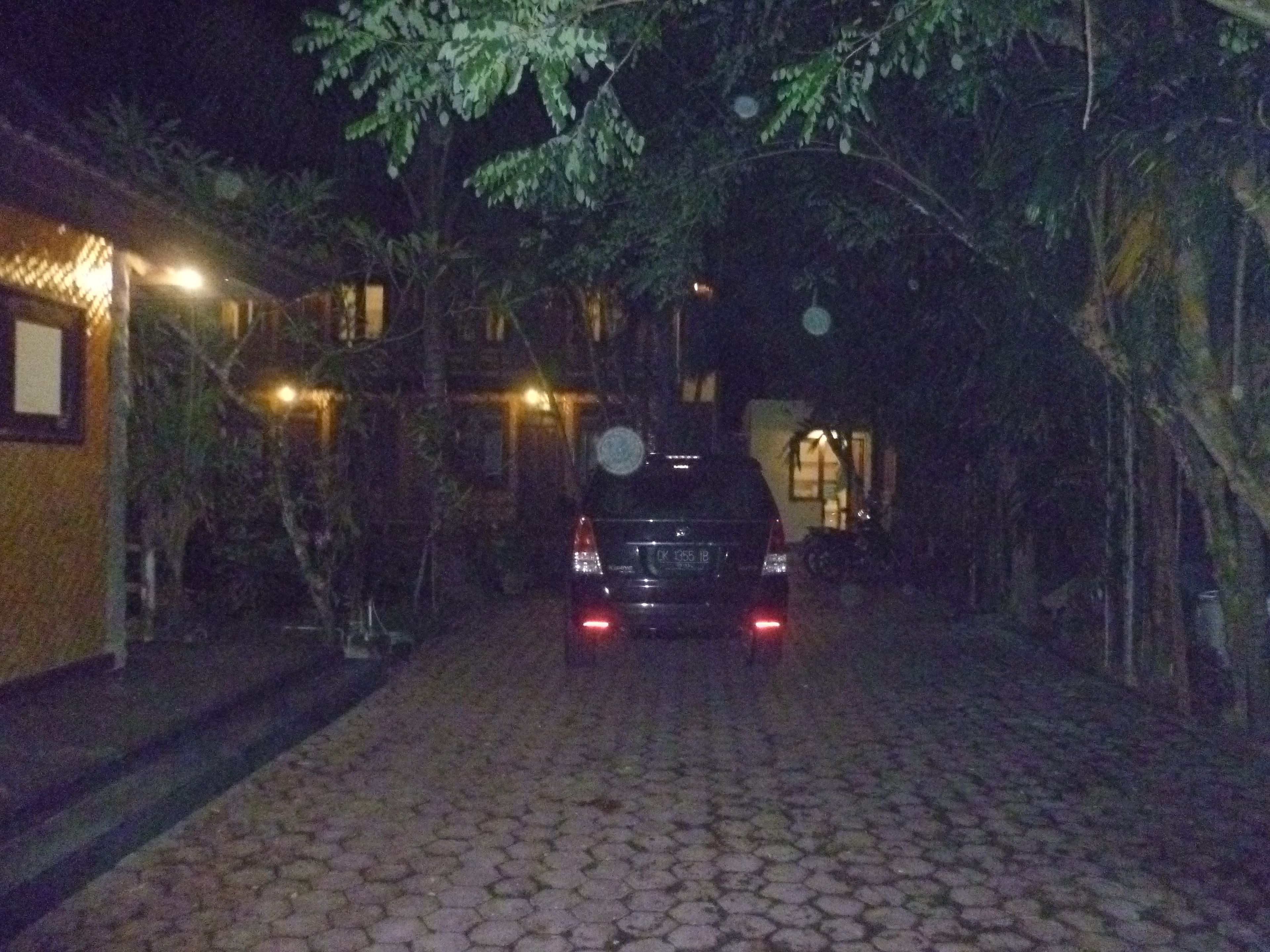 A nighttime scene of a paved pathway leading to a building with a car parked in front.