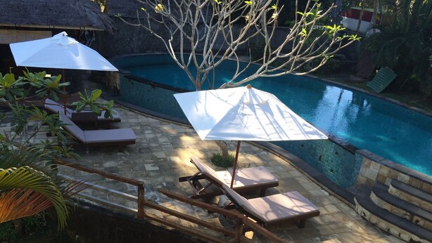 A poolside area with lounge chairs and umbrellas, a stone pathway, and a small bridge over a water feature. - Kangkung Cottages (Karangasem)