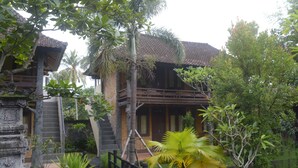 A traditional wooden building with a tiled roof, surrounded by lush greenery and a stone staircase leading to a wooden deck. - Kangkung Cottages (Karangasem)