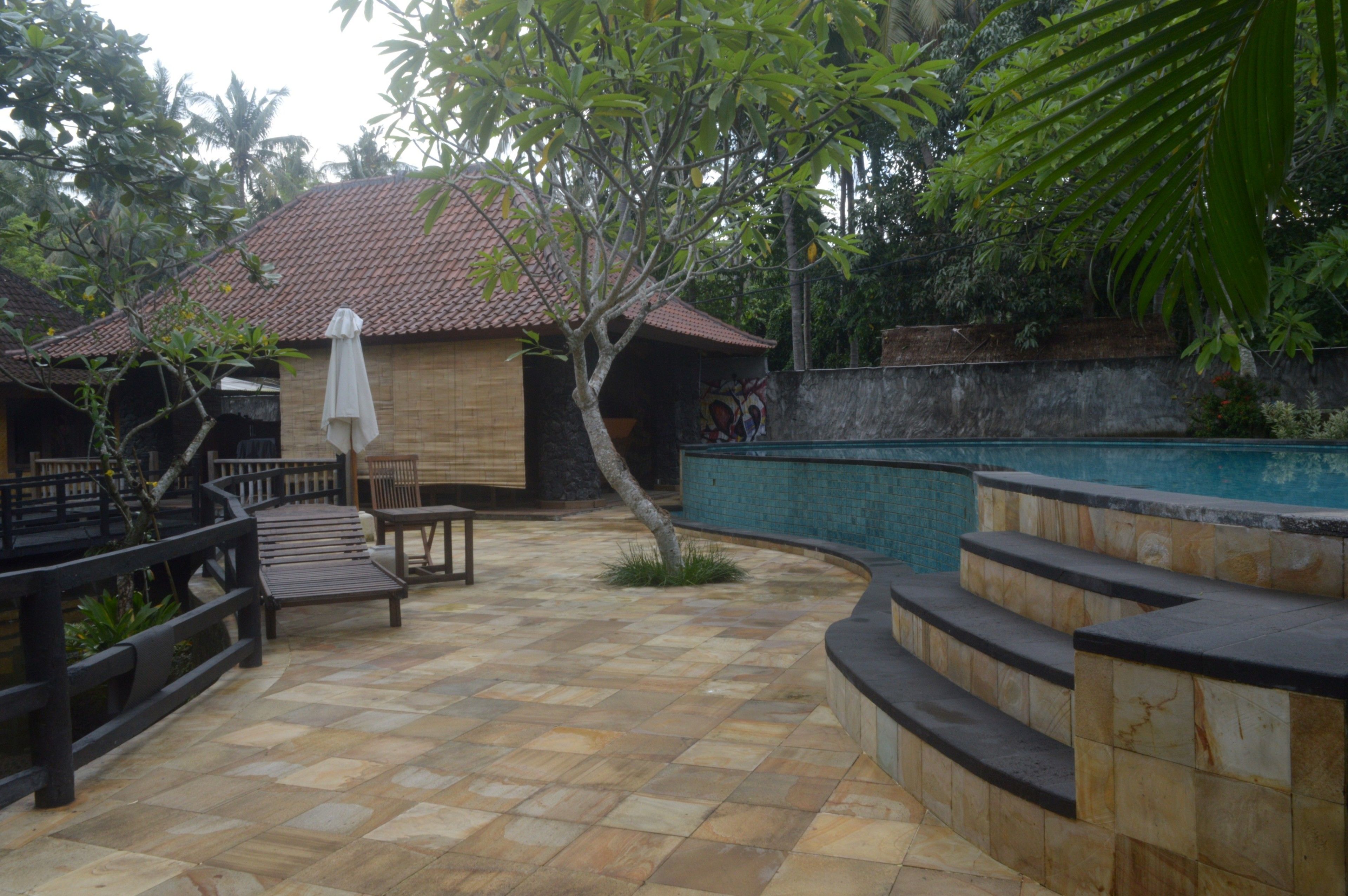 A courtyard with a tiled floor, a wooden bench, a small table, and a white umbrella.