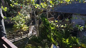 A wooden bridge over a pond with lush greenery and a thatched-roof structure in the background. - Kangkung Cottages (Karangasem)