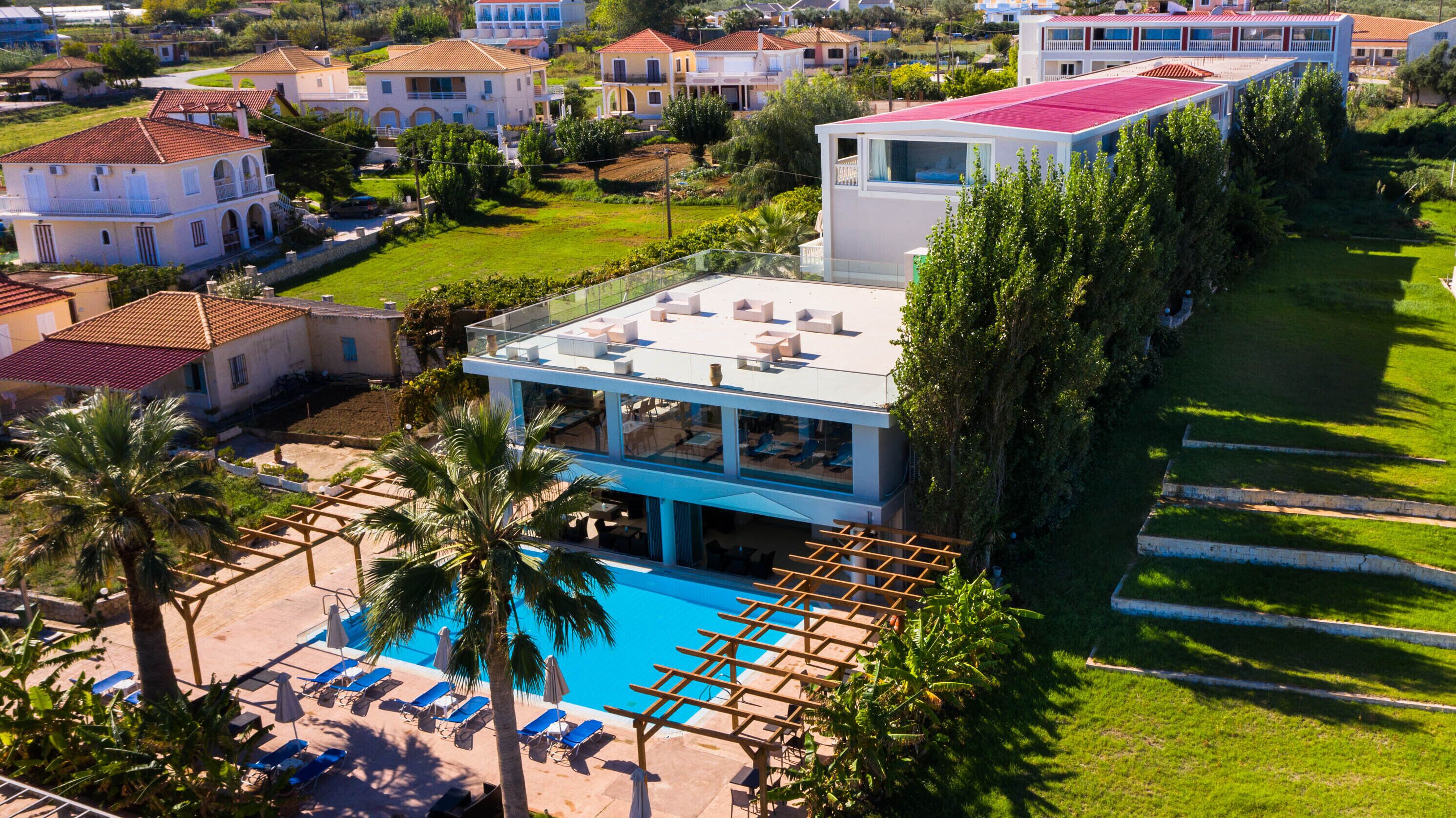 A modern hotel with a pool, sun loungers, and a view of surrounding houses.
