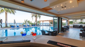 Un bar situé au bord de la piscine, proposant deux cocktails, avec vue sur la mer et des places assises en plein air.