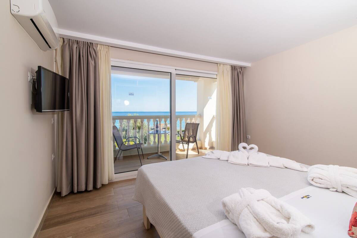 Une chambre d’hôtel avec un grand lit, une télévision à écran plat et un balcon offrant une vue sur la mer.