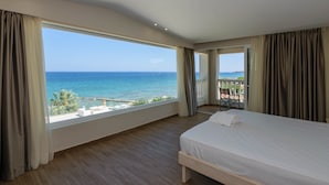 Une chambre d’hôtel dotée d’une grande fenêtre donnant sur la mer et d’un balcon.