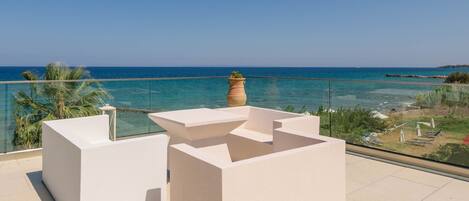 Un balcon offrant une vue dégagée sur la mer, un jardinier blanc et une balustrade en verre.