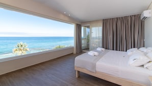 Une chambre avec une grande fenêtre donnant sur la mer, un lit avec du linge de maison blanc et un plancher en bois.