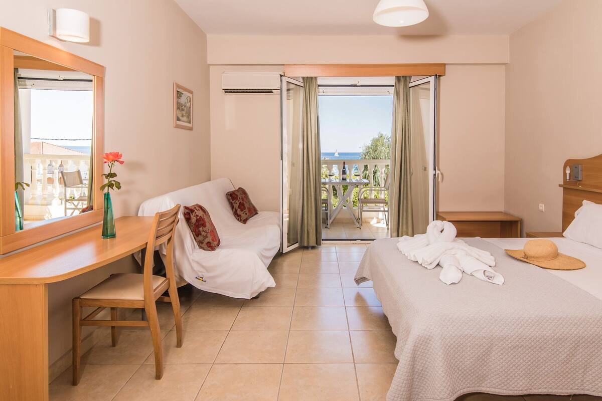 Une chambre d’hôtel avec un lit, un bureau, une chaise, un miroir et une vue sur le balcon extérieur.