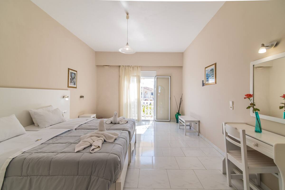 Une chambre d’hôtel avec deux lits, un bureau, une chaise, un miroir et une vue sur l’extérieur.