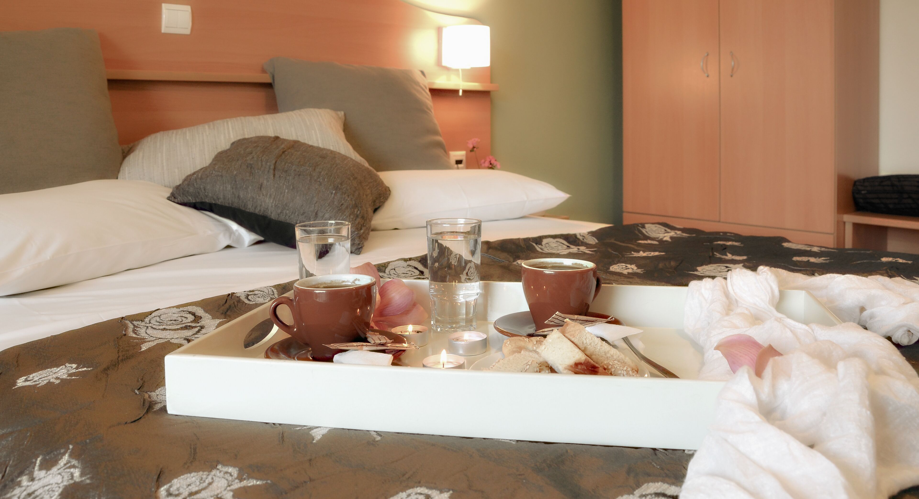 Una cama bien tendida con almohadas, una bandeja con alimentos para el desayuno y una taza de café.