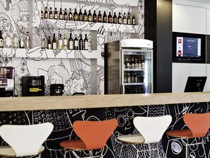 A bar area with a variety of liquor bottles, a refrigerator, and a TV screen displaying a tax change message. - Ibis Novo Hamburgo (Novo Hamburgo)