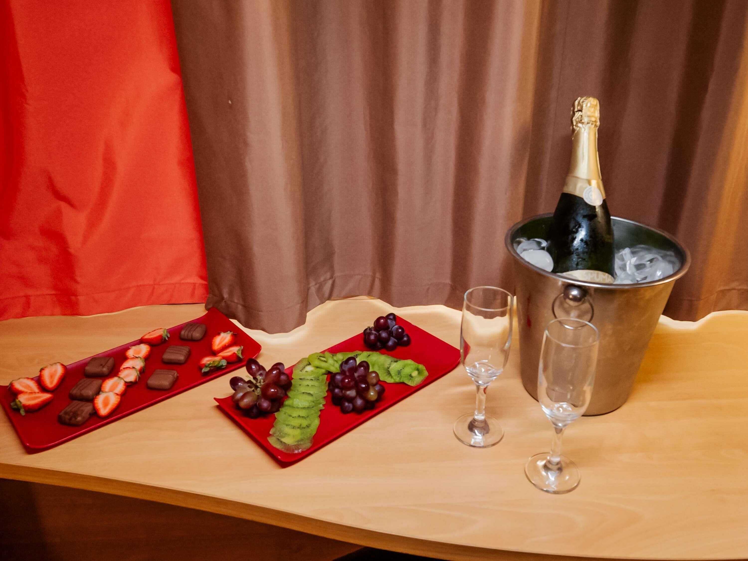 A table with a bottle of champagne, two glasses, and two red plates with strawberries and chocolate.