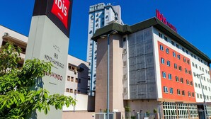 Un hotel con una fachada destacada en rojo y blanco, una estructura alta de diseño moderno, y un letrero que indica que pertenece a la cadena ibis.
