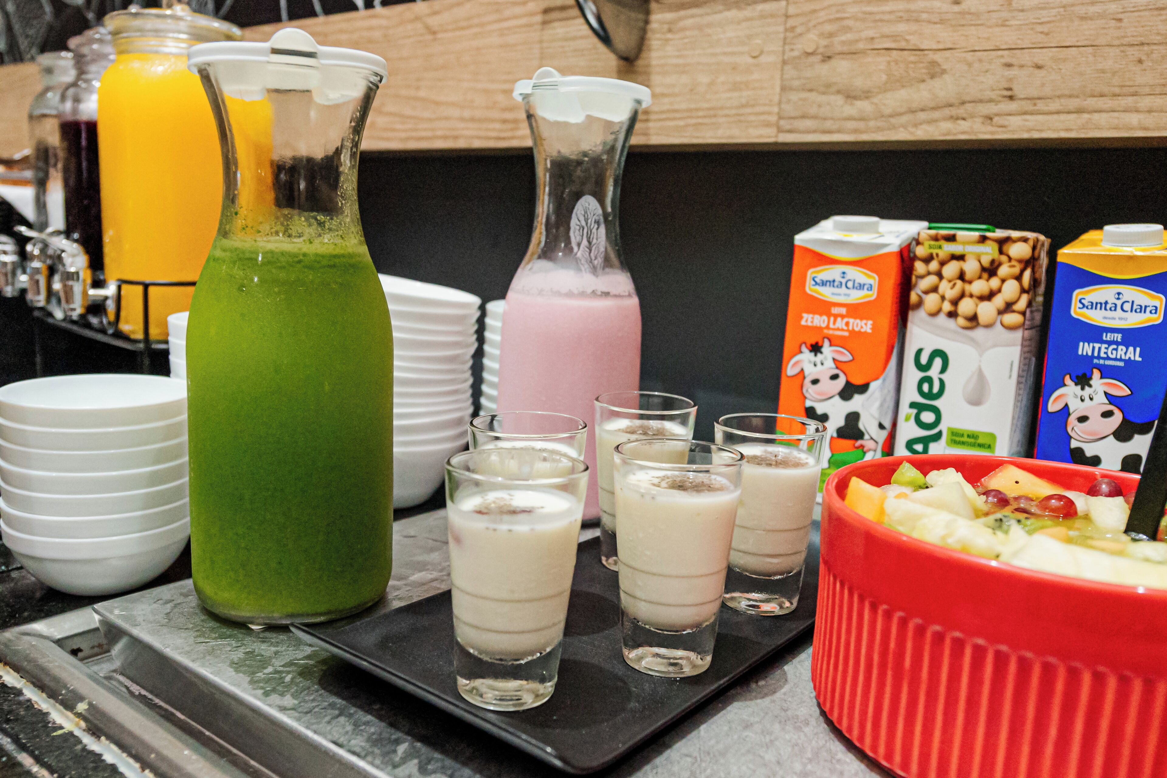 A kitchen counter with various food items and beverages, including a pitcher of green smoothie, a pink drink, and cartons of milk.