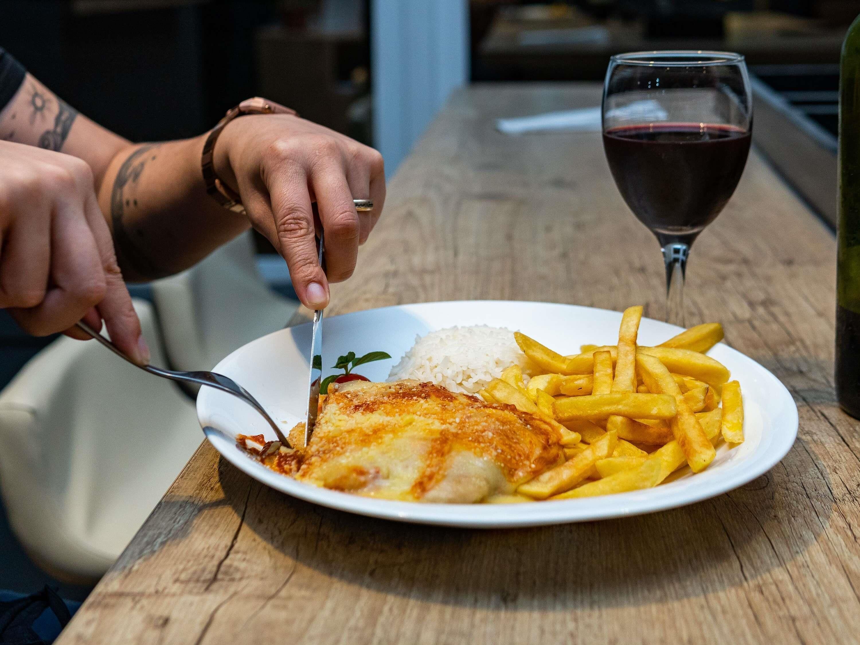 Un plato con pescado, arroz, papas fritas, una copa de vino tinto y una botella sobre una mesa de madera.