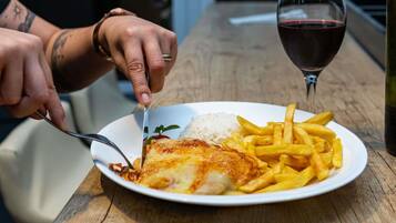 Un plato con pescado, arroz, papas fritas, una copa de vino tinto y una botella sobre una mesa de madera.
